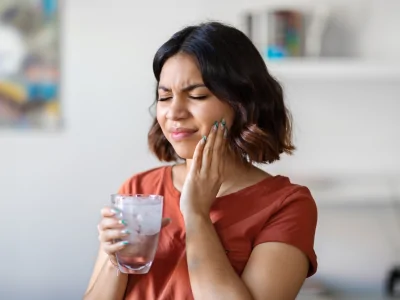 Woman wincing from tooth sensitivity while drinking cold water